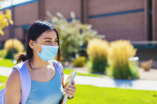 photo - College Student Walking on Campus and Wearing a Mask