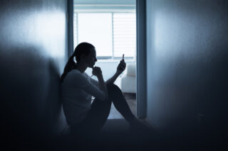 photo - distressed woman sitting on the floor at home with phone