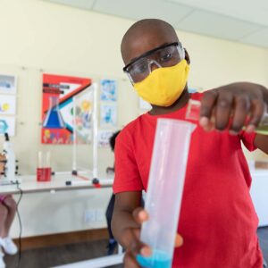 photo - Boy Wearing Face Mask and Protective Glasses Mixing Chemicals in Science Class