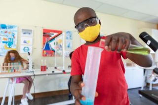 photo - Boy Wearing Face Mask and Protective Glasses Mixing Chemicals in Science Class