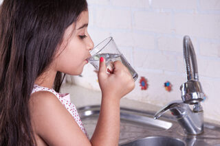 Little girl drinking water from kitchen faucet