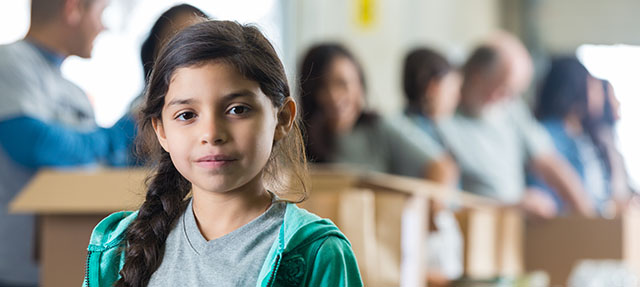 photo - Girl in Front of Line of Adults Packing Boxes with Food