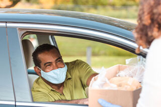 photo - Man in Car Wearing Mask and Picking Up Box of Food