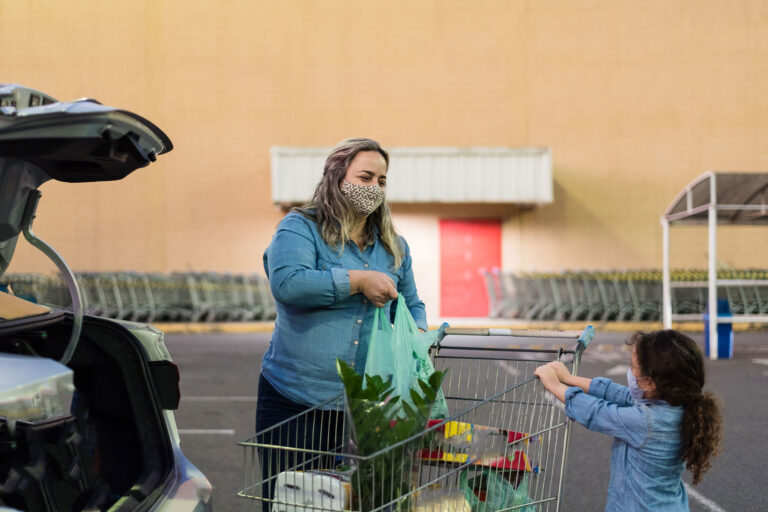 photo - Mother with Daughter Moving Groceries from Cart to Trunk of Car