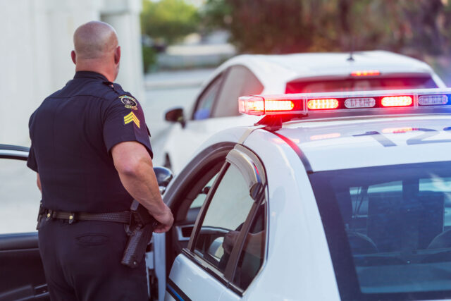 photo - Police Officer Getting Out of Police Car After Pulling Over Driver