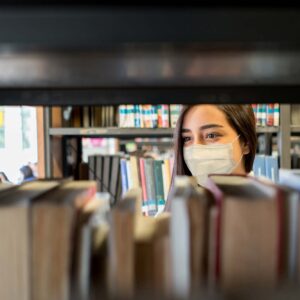 photo - Student Wearing a Facemask at the Library While Looking for a Book