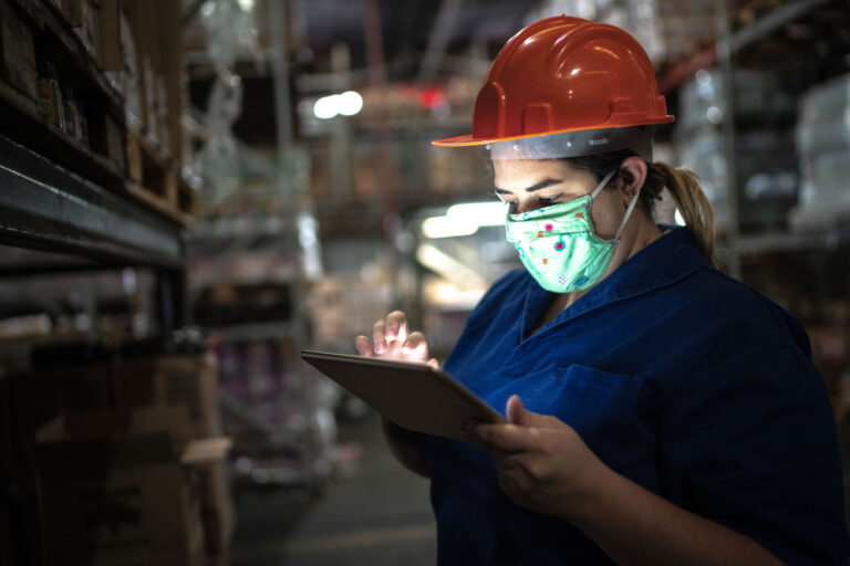 photo - Warehouse Worker Wearing Hard Hat and Mask while Working on Tablet