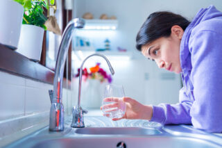 photo - Woman Is Waiting for Last Drop of Water from a Tap