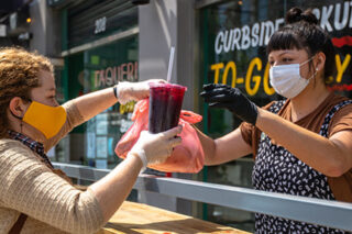 Photo of a restaurant worker handing customer takeout in masks