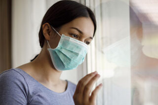 photo - Young Woman Wearing Mask and Looking Out Window