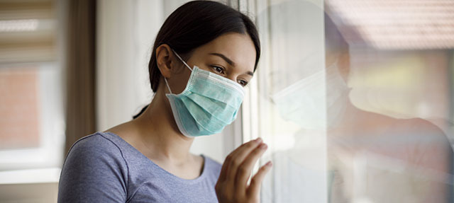 photo - Young Woman Wearing Mask and Looking Out Window